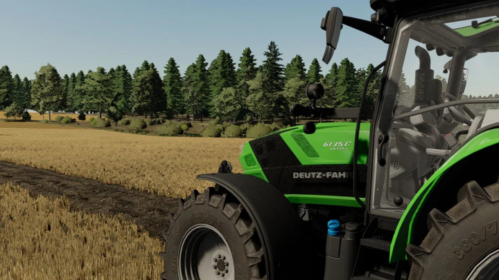 Deutz Fahr 6135C trekker mod in FS22, geparkeerd naast een tarweveld met weelderig bos op de achtergrond.