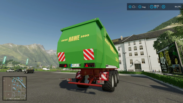 Mod FS22 Hawe csw 5000 v2.0.0.0 in Farming Simulator 22, con rimorchio verde in ambiente urbano con montagne sullo sfondo.