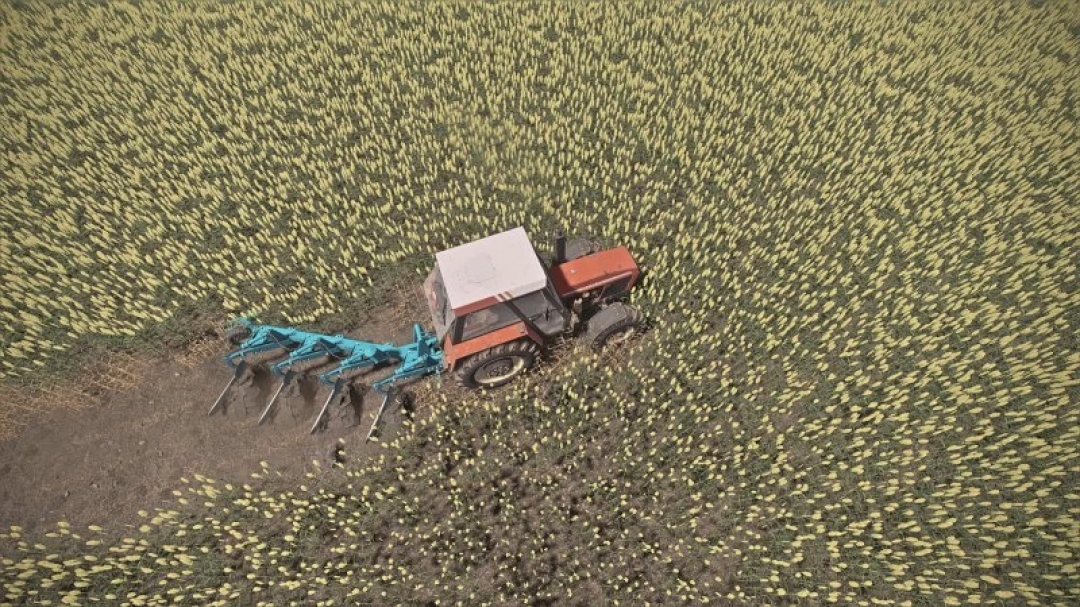 FS22 Overum 4 mod v1.0.0.0 in Farming Simulator 22 toont een tractor die een veld ploegt.