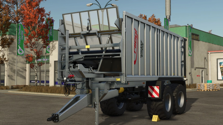 fs25-mods,  FS25 mod Fliegl ASW 271 przyczepa na parkingu, jesienne drzewa i budynek w tle.