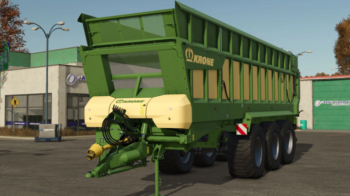 fs25-mods,  Krone GX520 trailer mod in FS25, met groen-gele ontwerp tegen een boerderijwinkel achtergrond.