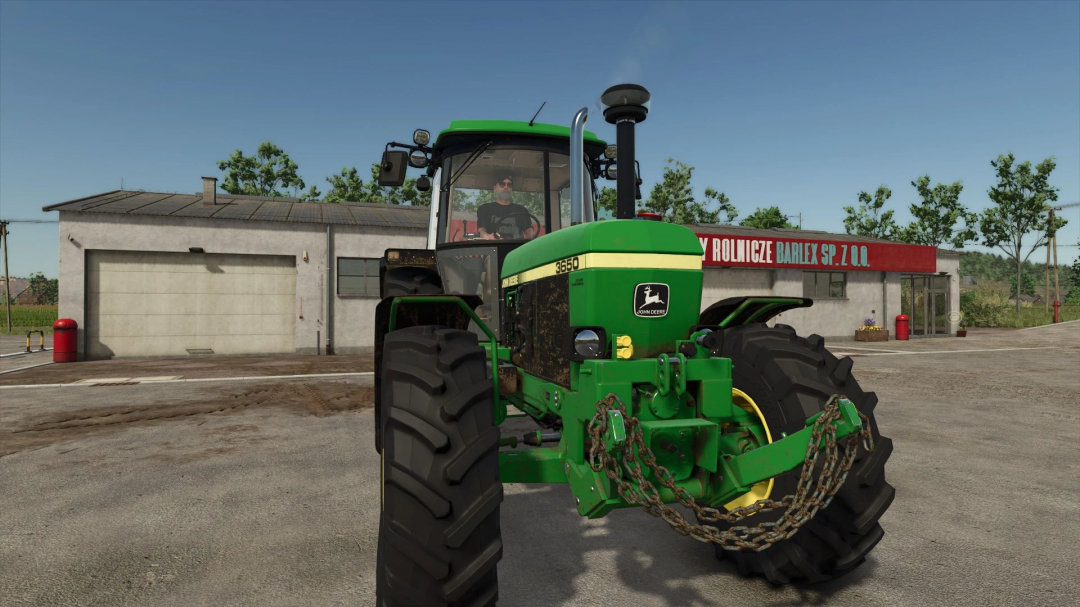 FS25 mod showing a green tractor with chains in front of a rural building.