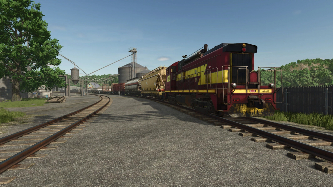 Train Stop mod in FS25 showing a locomotive and freight cars on tracks near a rural station.