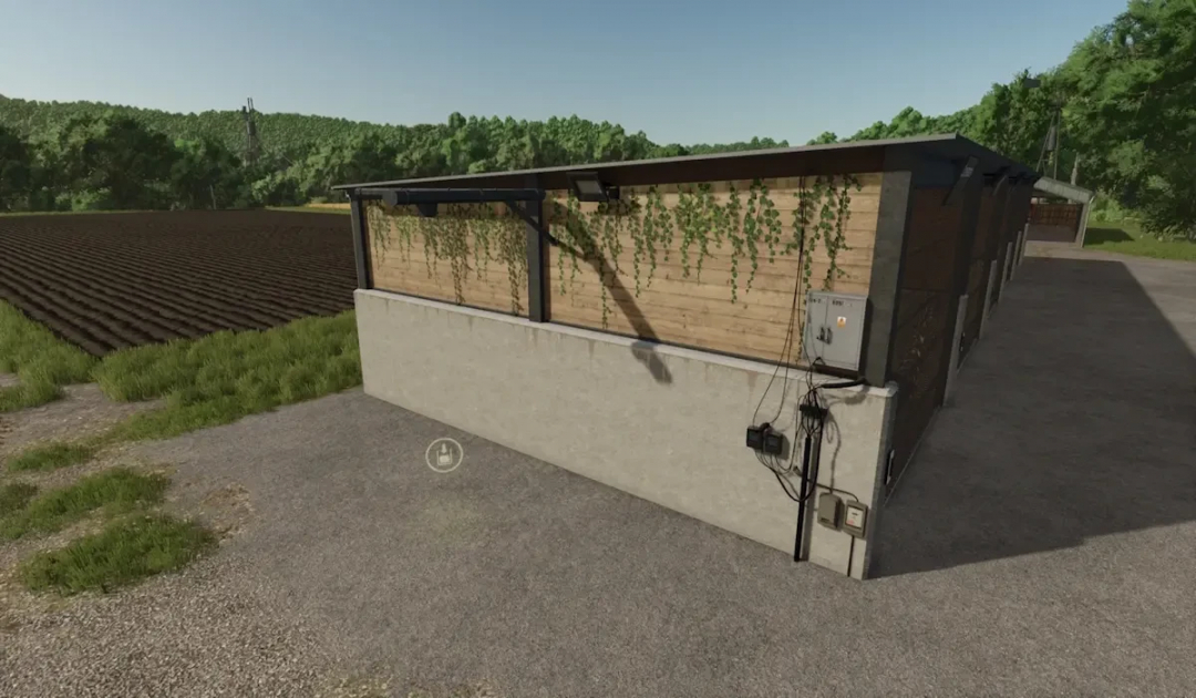 FBM25 Bulk Hall mod for FS25 showing a wooden building with greenery, beside a plowed field.