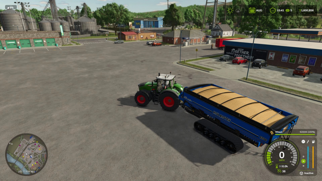 FS25 mod Enhanced Capacity v1.0.0.1: tractor hauling a full wheat trailer in a busy town setting.