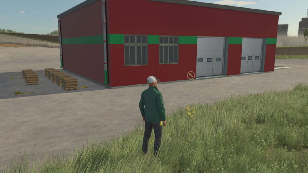 Player stands near Soja Factory in FS25 mod, featuring red-green building with crates outside.