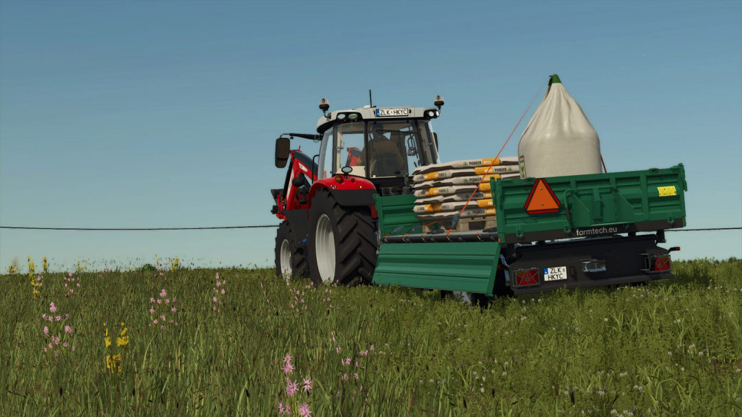 FS25 mod Farmtech EDK 650 trailer loaded with supplies, connected to a red tractor in a field. Farming Simulator 25 mods.