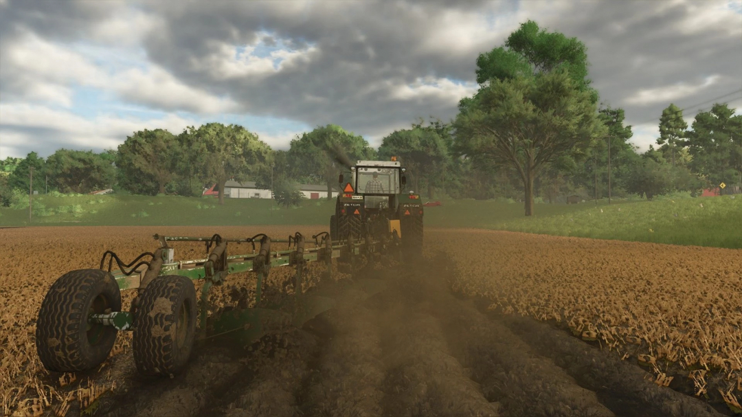 Tractor using PHX Pack mod in FS25 to plow a field under cloudy sky.