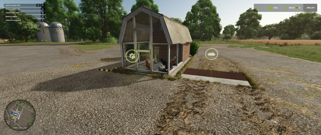 FS25 mod Chicken Coop v1.0.0.0 in a farm setting with trees and silos, featuring a wire-mesh enclosure for chickens.