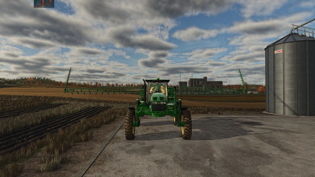 FS25 mod John Deere 4730 tractor in a field with silos and cloudy sky in the background.