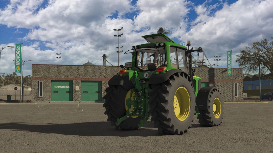 John Deere 6x20 tractor mod in FS25, parked beside Motorex building under cloudy sky.