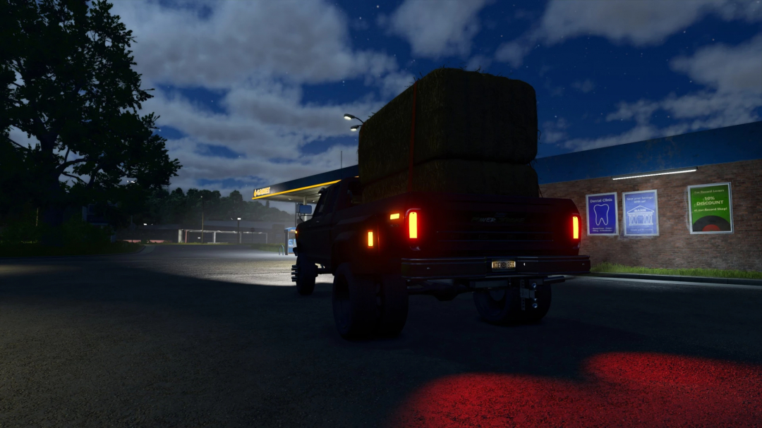 Night scene of a 78 Ford F350 with hay bales near a gas station in FS25 mod.