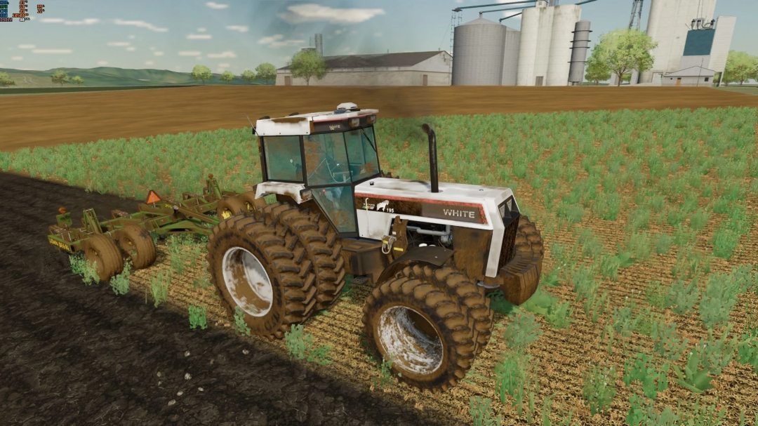 White Workhorse Series tractor mod in FS22 plowing a field with silos in the background.