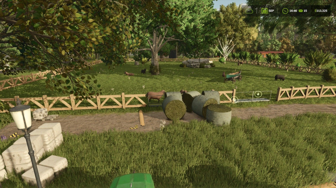 Small sheep and goat pasture with wooden fence in FS25, featuring hay bales and lush greenery.