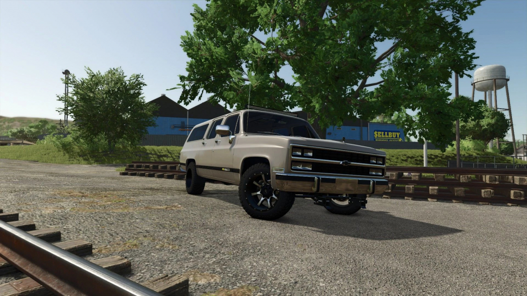 1990 Chevrolet Suburban 4x4 mod in FS25, showcasing a vintage SUV on a rural landscape with trees and a water tower.