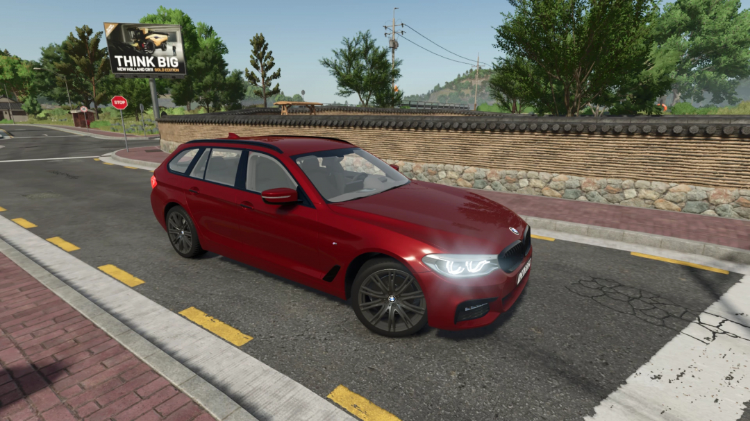 Red BMW 5 Touring G31 mod in FS25, driving on a countryside road with a stone wall and billboard.