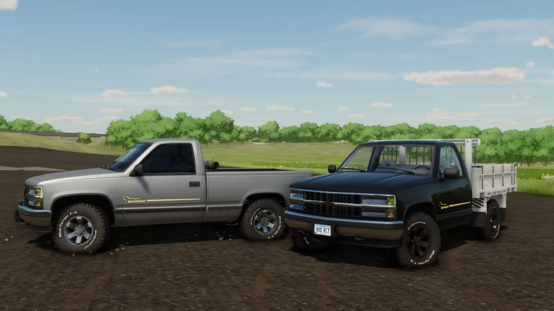 Two Chevrolet Silverado trucks in Farming Simulator 22 mod, one silver and one black, parked on a dirt path with green trees in the background.