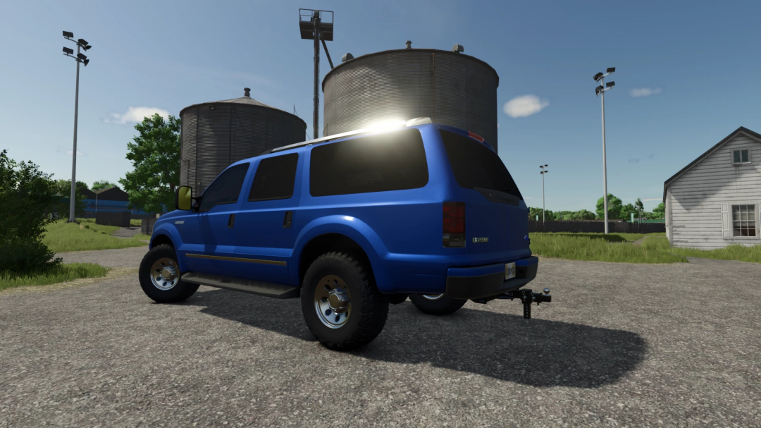 Blue 2005 Ford Excursion mod in FS25, parked near silos on a sunny day.