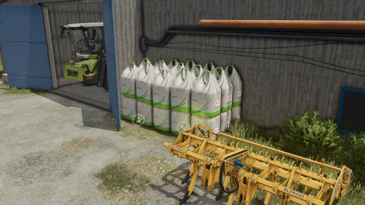 fs25-mods,  BigBag Tank mod in FS25, showcasing large sacks and farming equipment by a barn.