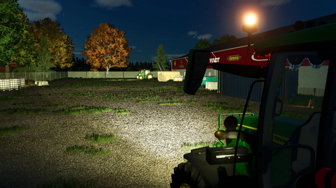 Night view of a farm in FS25 with a John Deere tractor, trees with autumn foliage, and lit machinery barn.