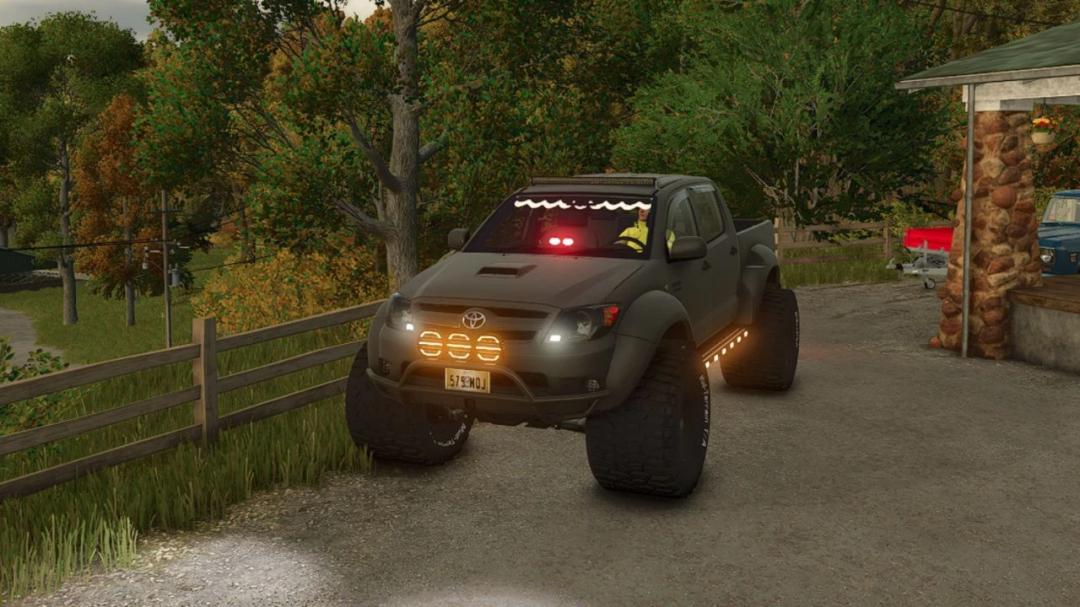 Toyota Hilux AT38 Edit v1.0.0.0 mod in FS25 with off-road lights, on a farm path.