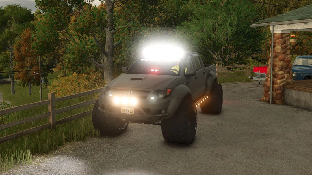 Toyota Hilux AT38 Edit mod for FS25, featuring an off-road vehicle with bright lights on a rural path.