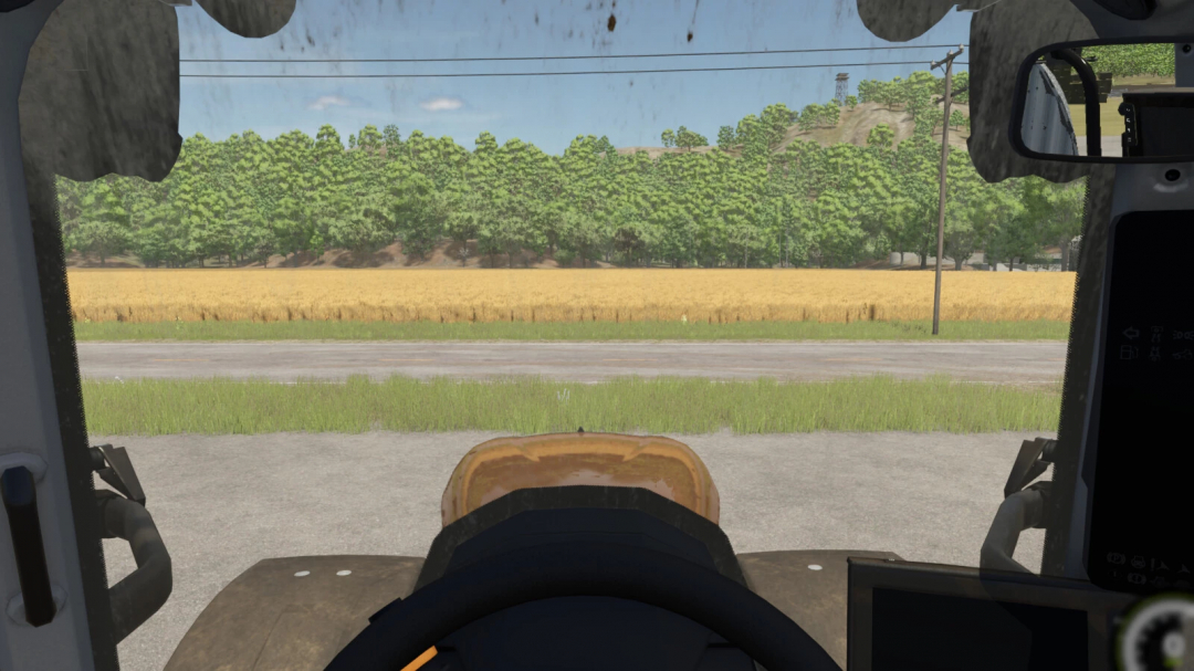 View from inside a tractor cab using Indoor Camera Position mod in FS25, overlooking a field and trees.