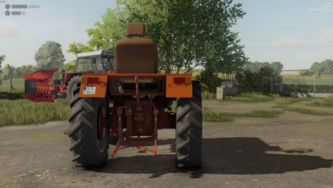 FS22 W?adzio T25 edit v1.0.0.0 mod showcasing a tractor with red implement, set in a rural environment with trees in Farming Simulator 22.