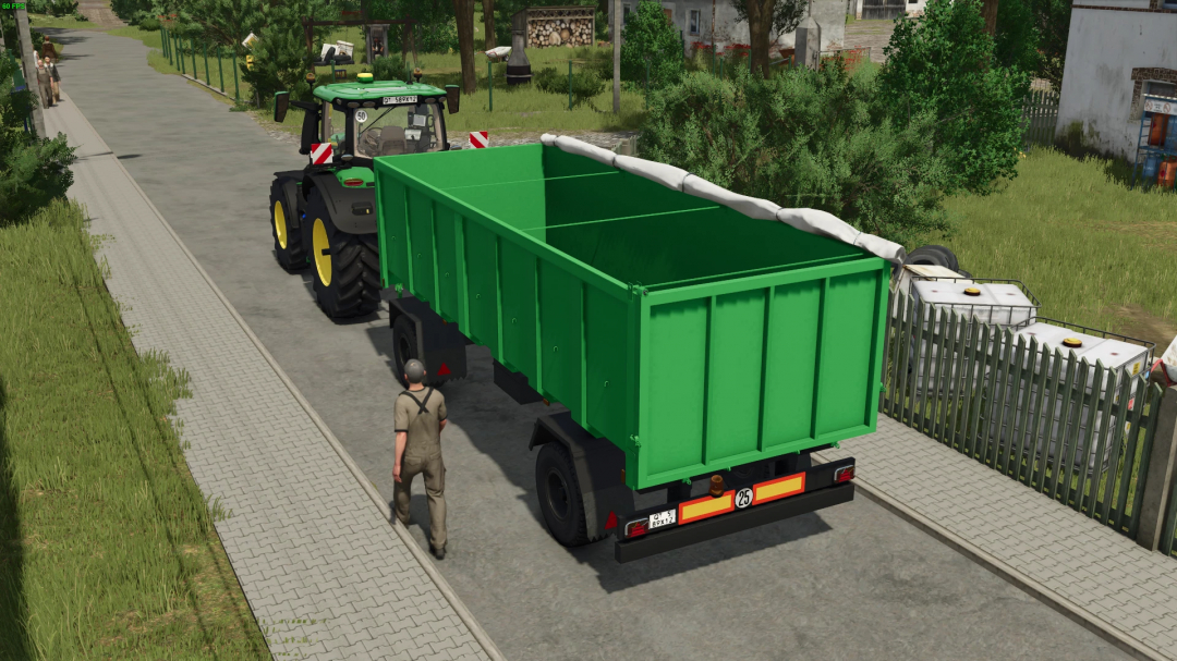 FS25 mod Selfmade Trailer 18t attached to a tractor, depicted on a paved rural road, showcasing a green container and surrounding greenery.