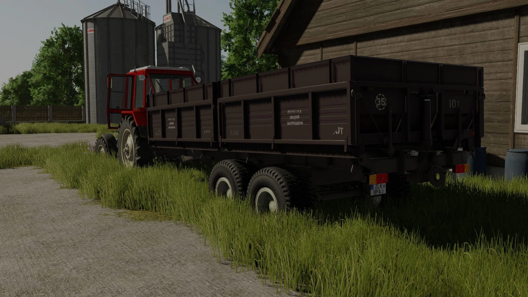 Farming Simulator 25 mod: a red tractor with a black Fliegl VFW 10600 trailer parked beside a wooden building, with silos in the background.