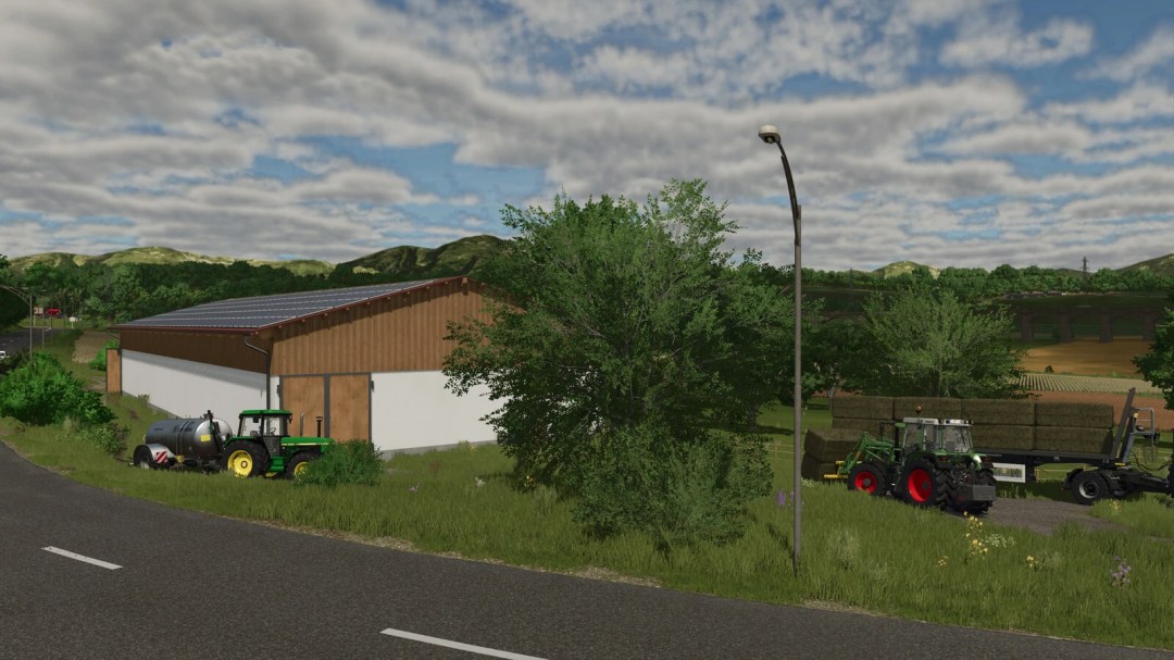 Farming Simulator 25 mod: Bavarian Cowshed v1.0.0.1 near farm equipment and hay trailer in a rural landscape.