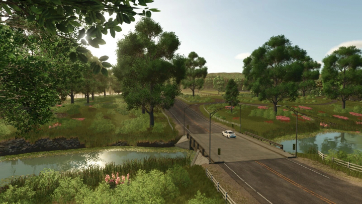 fs25-mods, Scenic view of a countryside road crossing a small bridge with green trees and water, from Farming Simulator 25 with New American v1.0.0.0 mods.