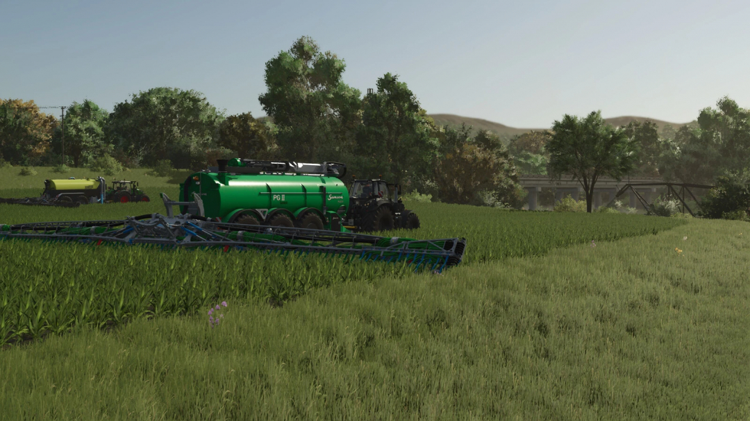 Farming Simulator 25 mod scene featuring a green slurry distributor tanker working on a field with trees and a bridge in the background.