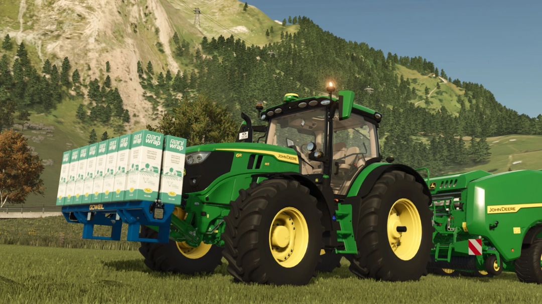 Farming Simulator 25 mod: John Deere tractor with Rani Wrap mod, featuring green and yellow design, set in a grassy field with mountains in the background.