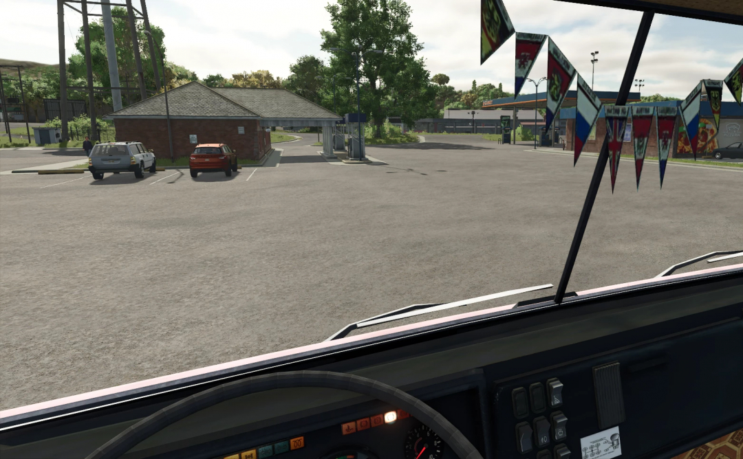 View from inside a truck in Farming Simulator 25, showing a parking lot and gas station with trees and vehicles in the background.
