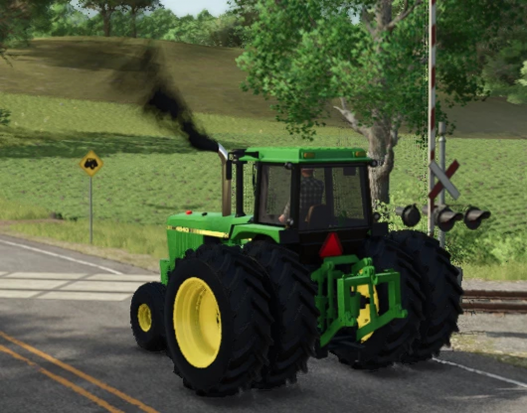 Farming Simulator 25 mod: Green John Deere 4840 tractor on a rural road, emitting black smoke, with trees and a railroad crossing in the background.