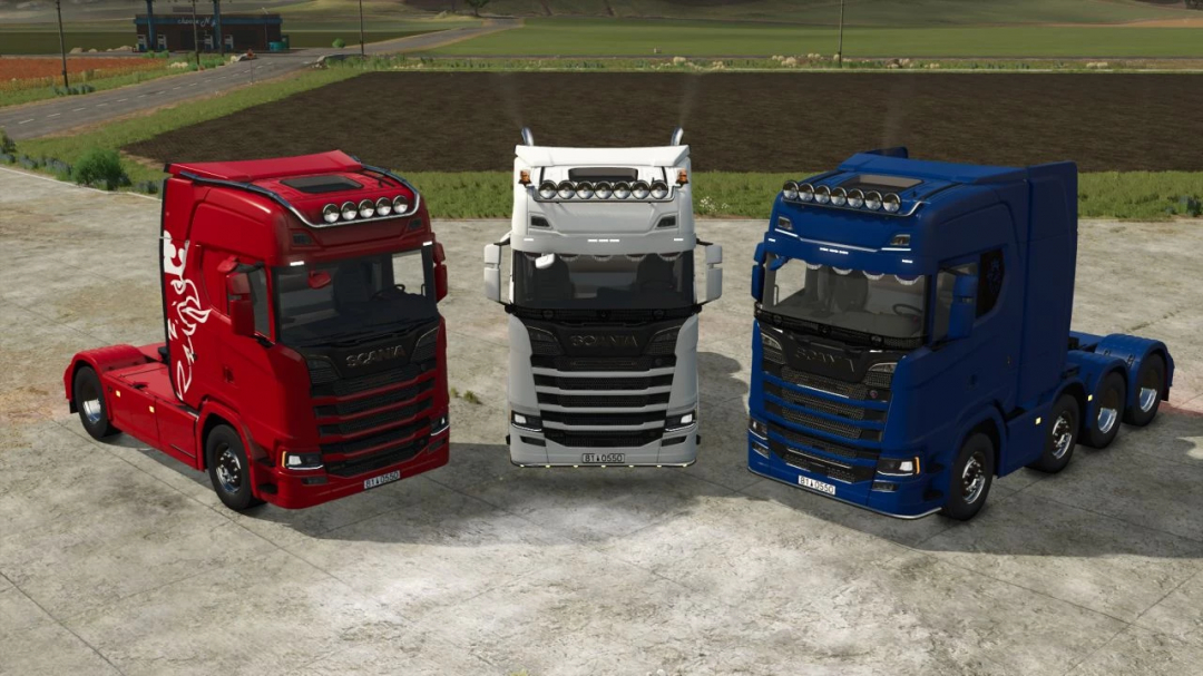 Three Scania S trucks mod from Farming Simulator 25, in red, white, and blue, parked on a farm with fields in the background.