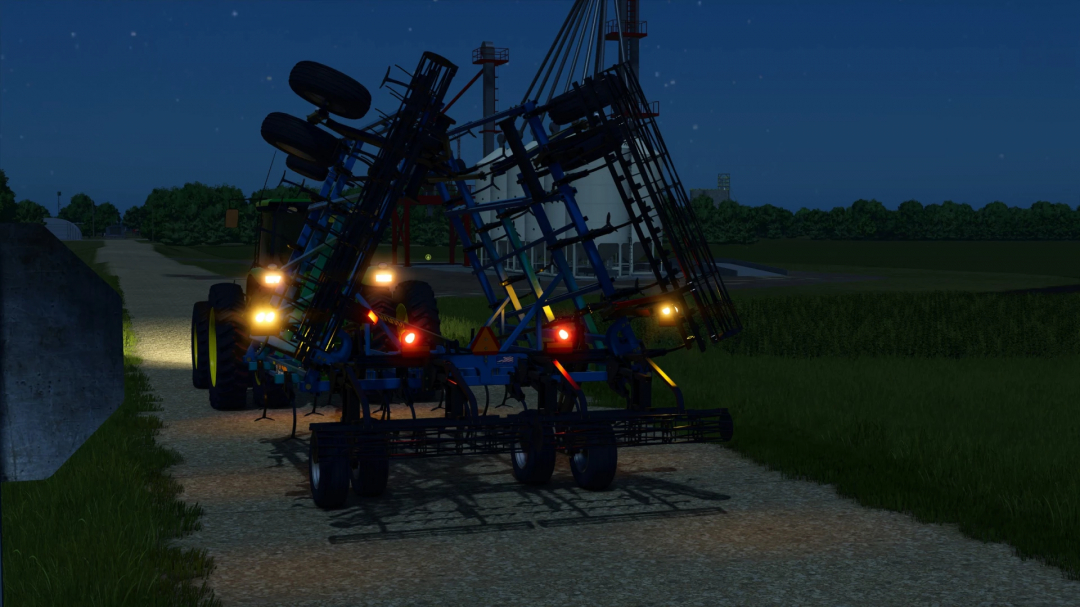 Farming Simulator 25 mod: DMI Tigermate II implement on a tractor at night, glowing lights, on a farm road, with fields and a grain silo in the background.