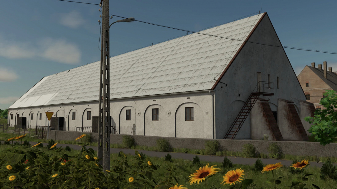 Farm building in Farming Simulator 25 with a large white barn and outdoor staircase, surrounded by sunflower plants and greenery.