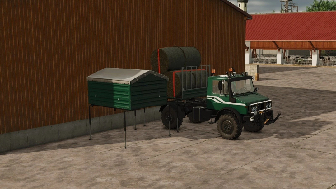 Farming Simulator 25 mod: Green utility vehicle with hay bales and storage trailer parked near a barn and outdoor seating area.